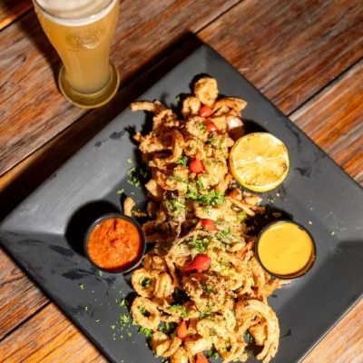Crispy fried calamari appetizer with dipping sauces and lemon served with a glass of beer on wooden table