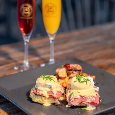 Eggs Benedict with hollandaise sauce and roasted potatoes served with mimosas on rustic wooden table