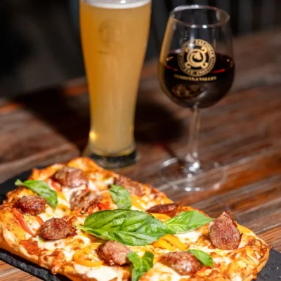 Flatbread pizza with sausage and fresh basil served with beer and red wine on rustic restaurant table