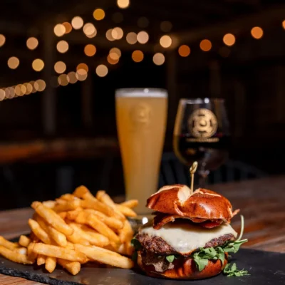 Gourmet cheeseburger with fries served on slate board with beer and wine in cozy restaurant setting