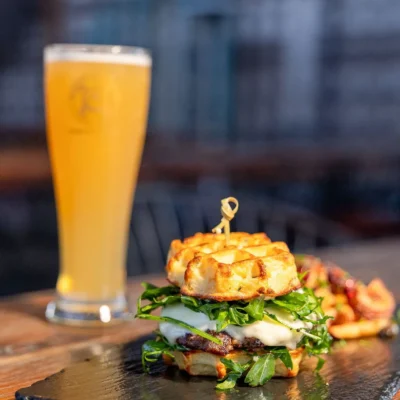 Gourmet mini burger with melted cheese and arugula served on slate board with a glass of craft beer in background