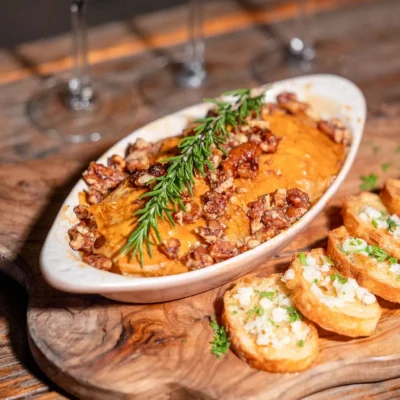 Creamy whipped cheese dip topped with candied nuts and rosemary served with toasted crostini on wooden board